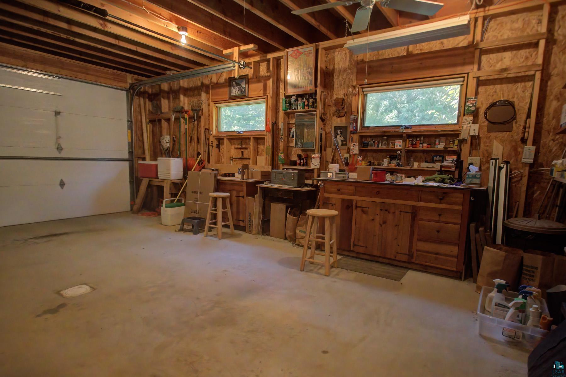 2811 Schaeffer Road Ely, MN 55731 - Photo 37 of 40 Exposed wood beam ceiling, concrete flooring, two windows, built-in wooden cabinetry with drawers, and an overhead garage door