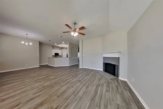 a view of an empty room with wooden floor and a kitchen