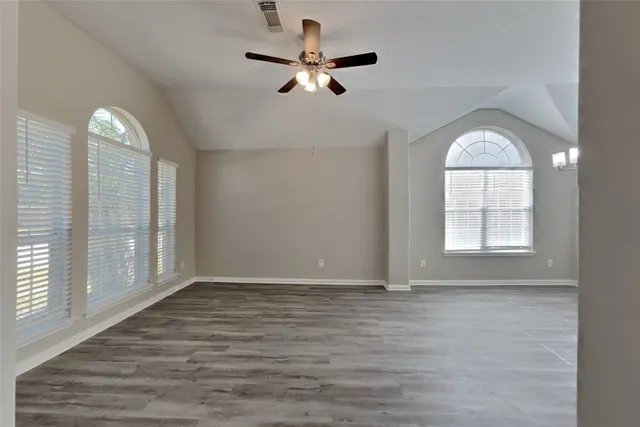 an empty room with wooden floor chandelier fan and windows