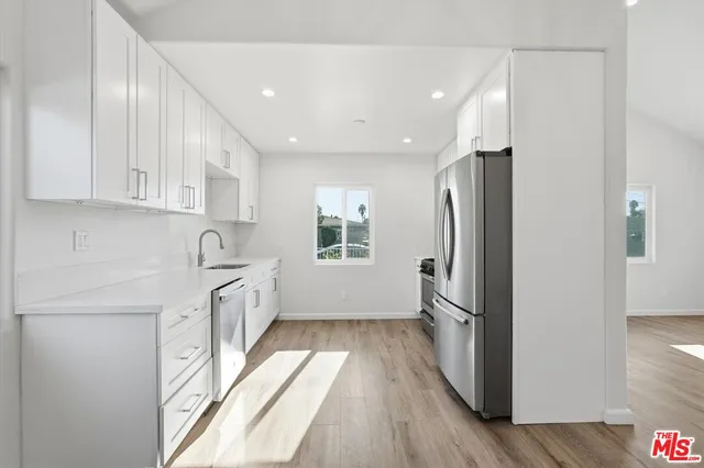 a kitchen with granite countertop a refrigerator a sink a stove a refrigerator and white cabinets with wooden floor