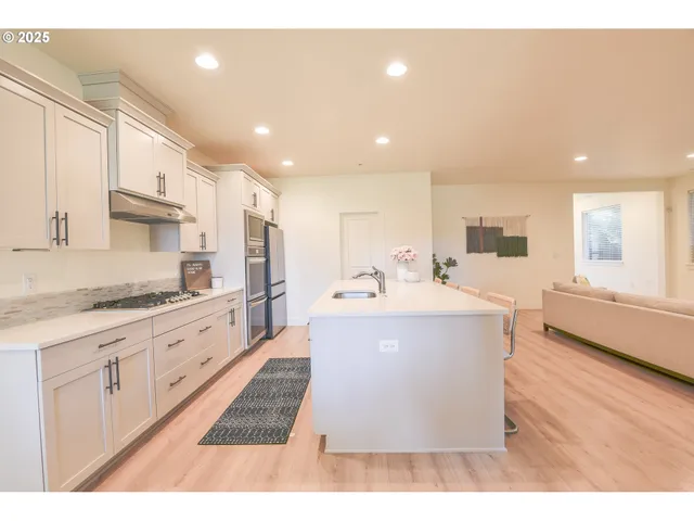 a large white kitchen with a large counter top space a sink stainless steel appliances and cabinets