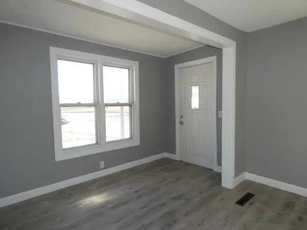 a view of an empty room with wooden floor and a window