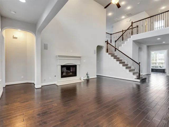 a view of an empty room with wooden floor staircase and a kitchen