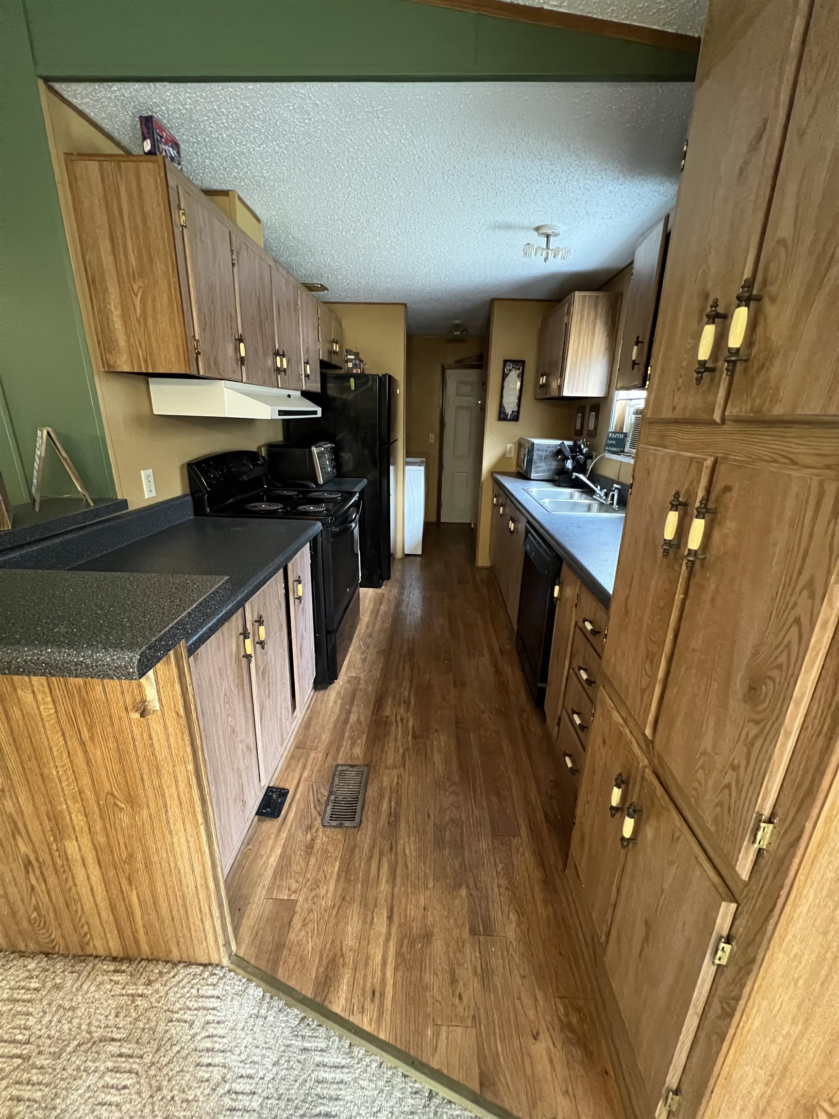 1405 Bruton Branch Road Savannah, TN 38372 - Photo 12 of 20 Kitchen featuring dark wood-style flooring, a textured ceiling, dark countertops, under cabinet range hood, and black appliances