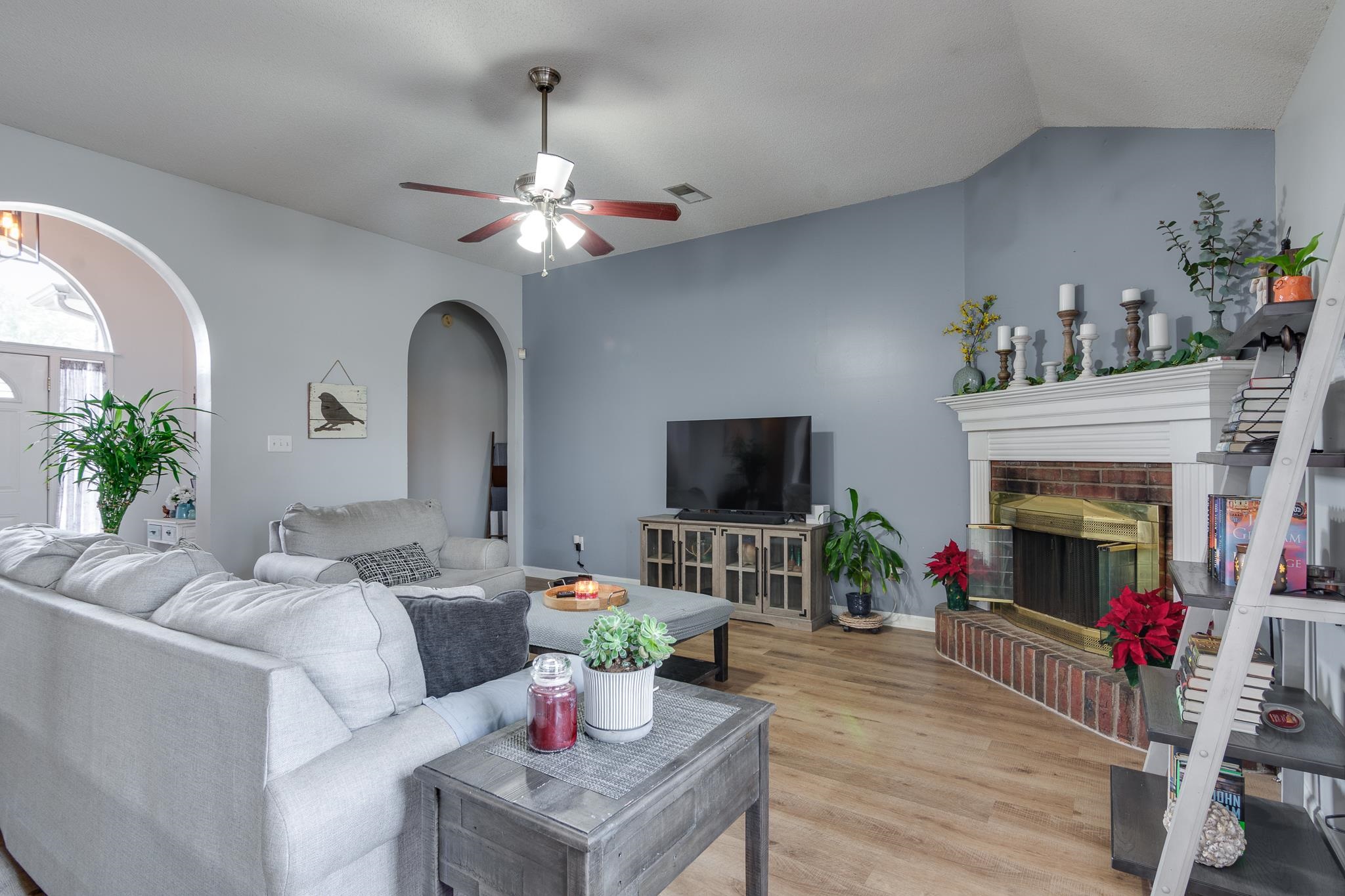 7314 Patsy Circle North Memphis, TN 38125 - Photo 3 of 28 Living room featuring a ceiling fan, light wood-style flooring, a brick fireplace, vaulted ceiling, and arched walkways