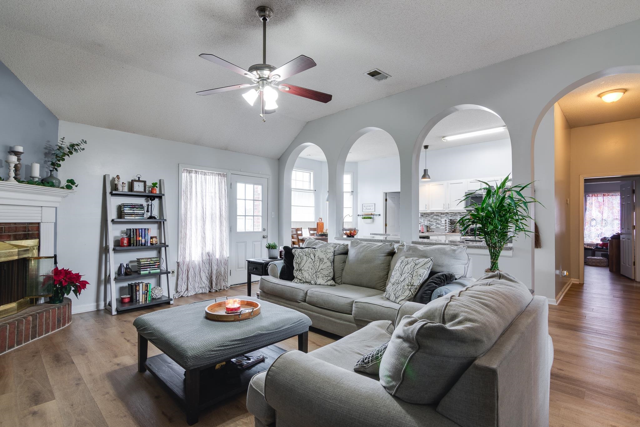 7314 Patsy Circle North Memphis, TN 38125 - Photo 8 of 28 Living room with a textured ceiling, a brick fireplace, vaulted ceiling, wood finished floors, and a ceiling fan