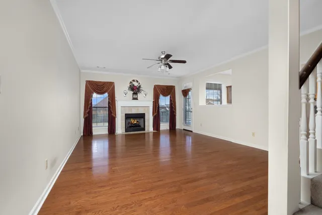 an empty room with wooden floor a ceiling fan a fireplace and windows