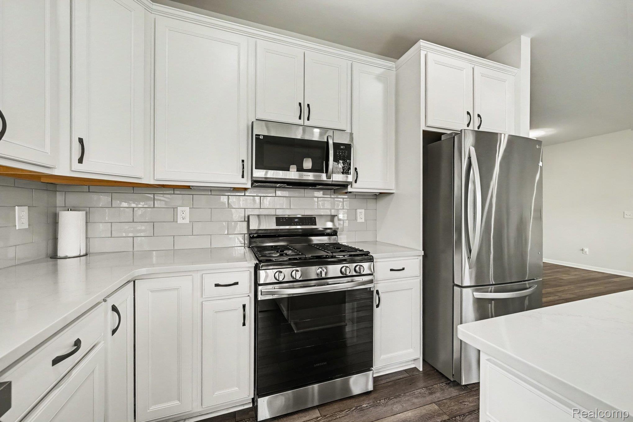 50153 Fowler Road Canton, MI 48188 - Photo 9 of 27 White cabinetry, stainless steel appliances, light-toned countertops, subway tile backsplash, and dark wood-finish flooring