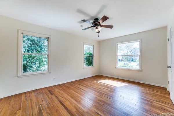 an empty room with wooden floor chandelier fan and windows