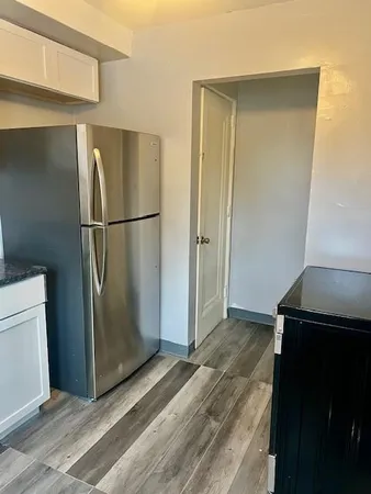 a view of a refrigerator in kitchen and an empty room with wooden floor