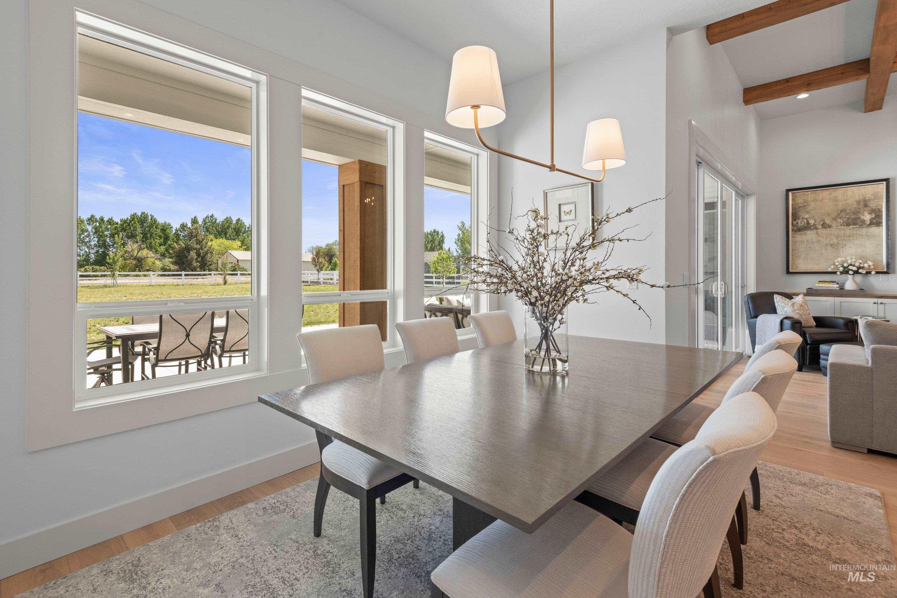 24990 Belgian Way Middleton, ID 83644 - Photo 16 of 50 Dining area with abundant natural light from multiple large windows, wood-finish flooring, a contemporary linear chandelier, and exposed ceiling beams