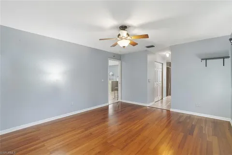 a view of an empty room with wooden floor and a ceiling fan