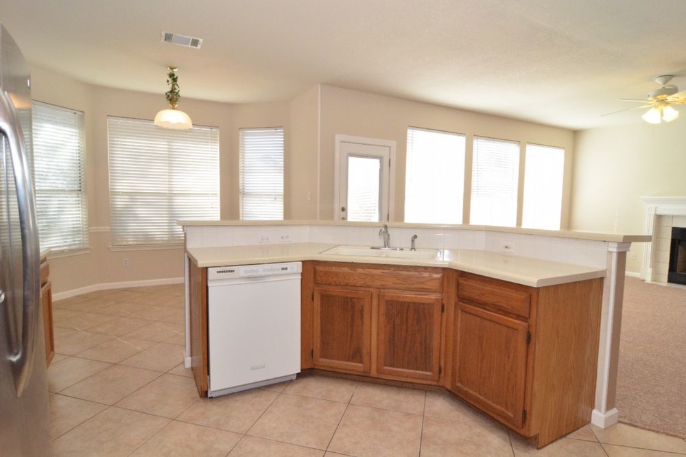 9405 Lightwood Loop Austin, TX 78748 - Photo 19 of 24 Kitchen featuring wood cabinetry, a white dishwasher, and a light-toned countertop with a breakfast bar