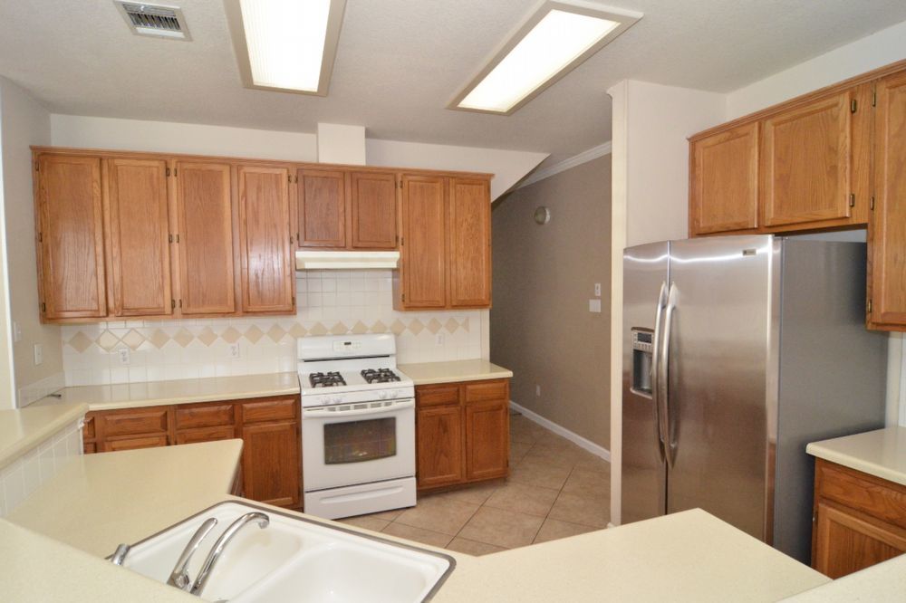 9405 Lightwood Loop Austin, TX 78748 - Photo 20 of 24 Kitchen featuring wood-finish cabinetry, light countertops, and a white gas range with overhead vent