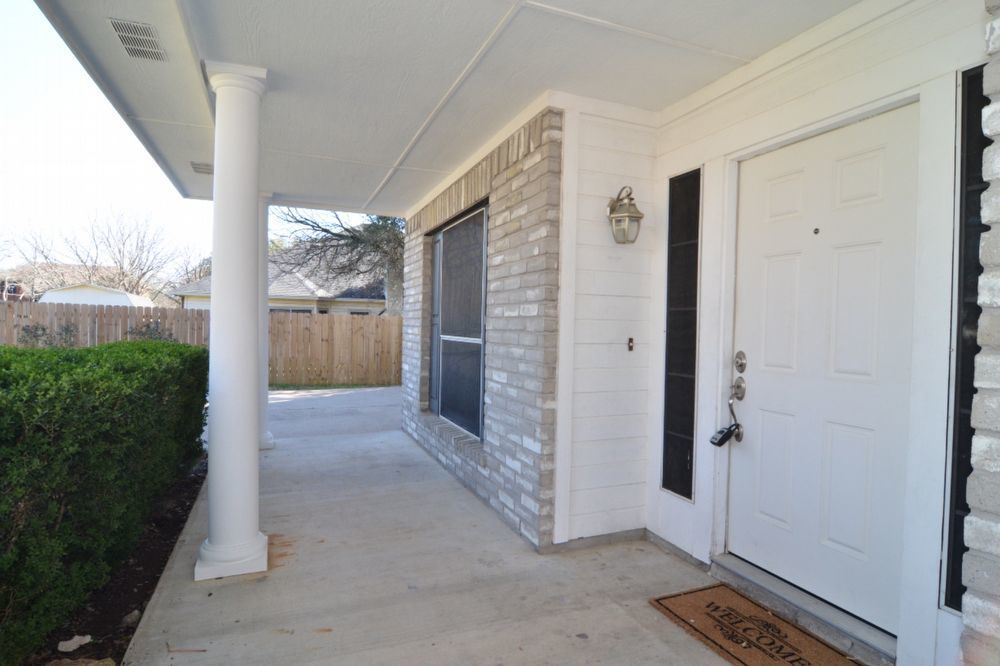 9405 Lightwood Loop Austin, TX 78748 - Photo 5 of 24 Covered front porch featuring a white paneled entry door, an exterior wall lantern, and light-toned brick siding