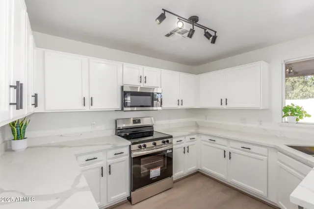 a kitchen with stainless steel appliances white cabinets a sink a stove and a window