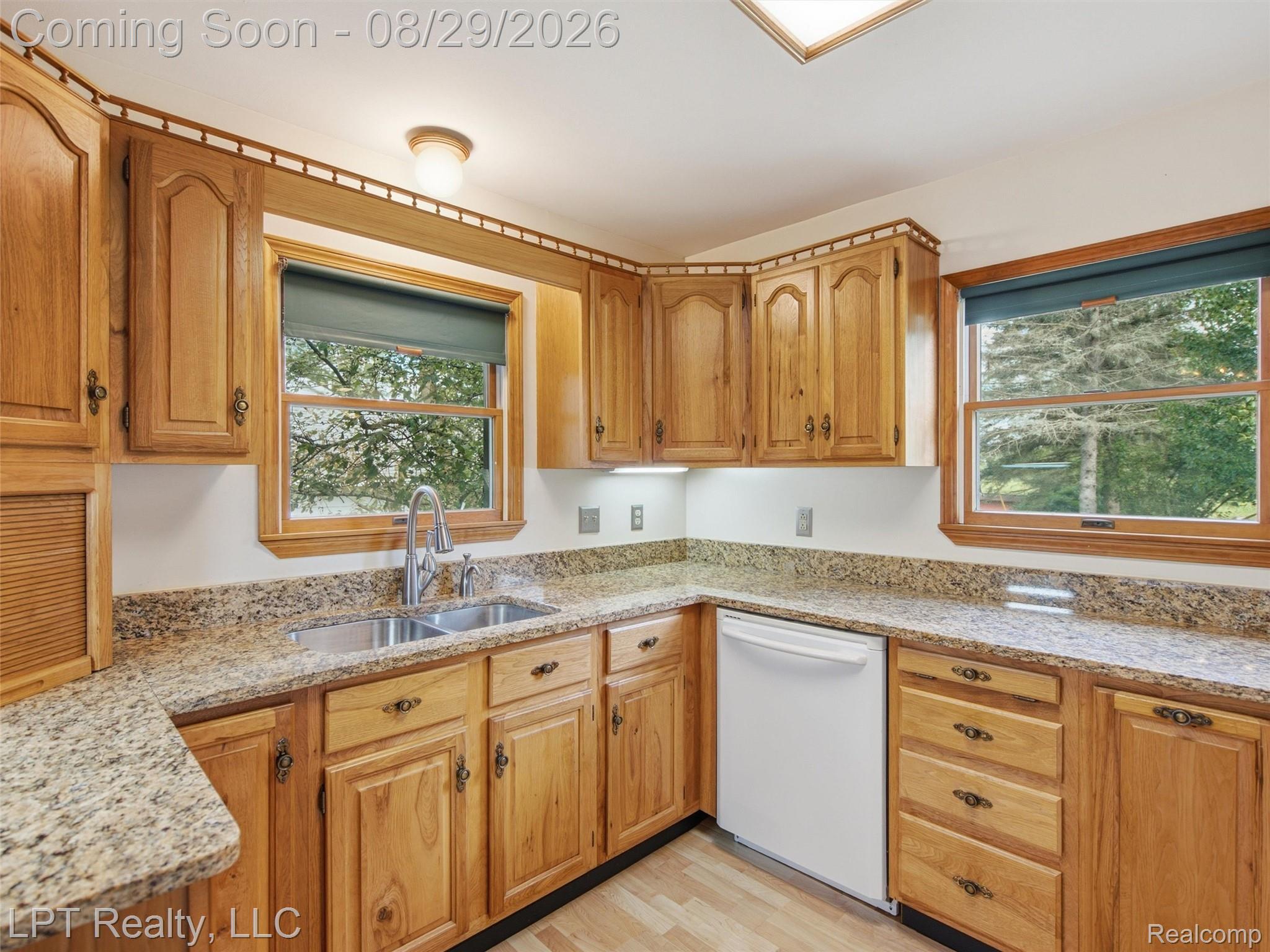 154 Bullis Road Gregory, MI 48137 - Photo 16 of 37 Kitchen featuring wood cabinetry, light-toned countertops, a double basin stainless steel sink, wood-finish flooring, and a white dishwasher