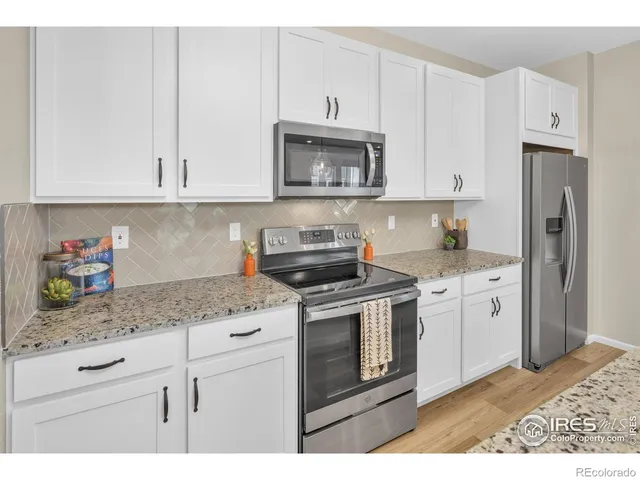 a kitchen with stainless steel appliances granite countertop a stove a sink and a white refrigerator with white cabinets