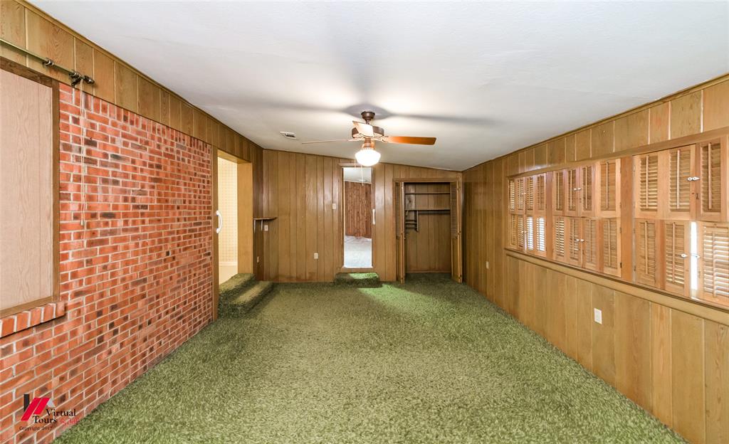 205 7th Street Northeast Springhill, LA 71075 - Photo 29 of 40 Brick accent wall, wood-finish paneling, green carpeting, built-in shelving, and ceiling fan