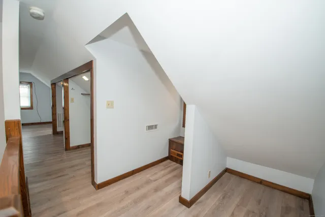a view of a hallway to an empty room with wooden floor and a window