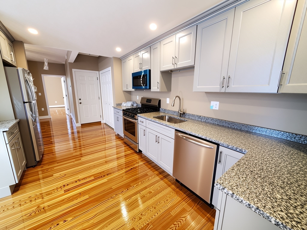 84 Cross Street Somerville, MA 02145 - Photo 11 of 42 a kitchen with stainless steel appliances granite countertop a refrigerator a sink dishwasher a stove and white countertops with wooden floor