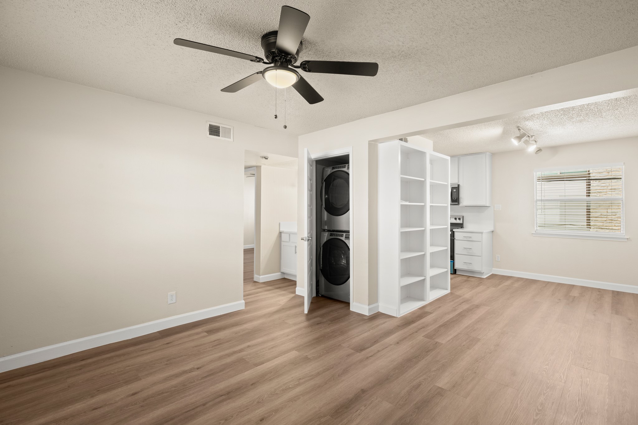 Unfurnished bedroom with a textured ceiling, light wood finished floors, ceiling fan, and stacked washing machine and dryer