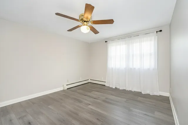 an empty room with wooden floor fan and windows