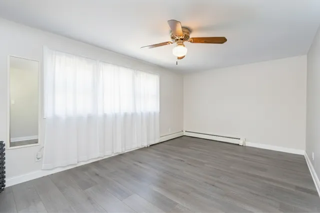 an empty room with wooden floor fan and windows