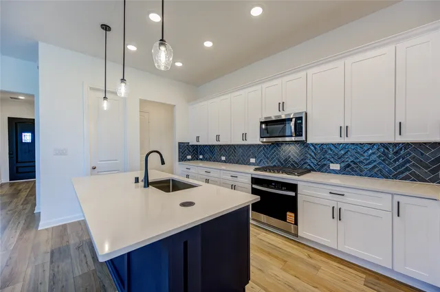 a kitchen with stainless steel appliances granite countertop a sink dishwasher stove and white cabinets with wooden floor