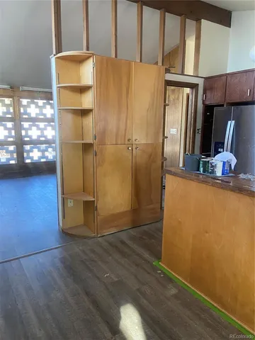 a view of a refrigerator in kitchen and an empty room with wooden floor