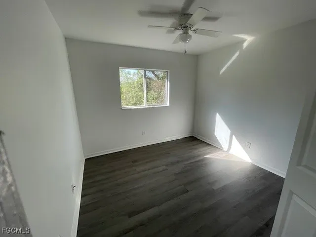 an empty room with wooden floor chandelier fan and windows