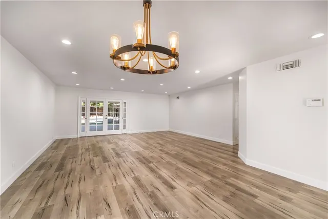 a view of an empty room with wooden floor and chandelier