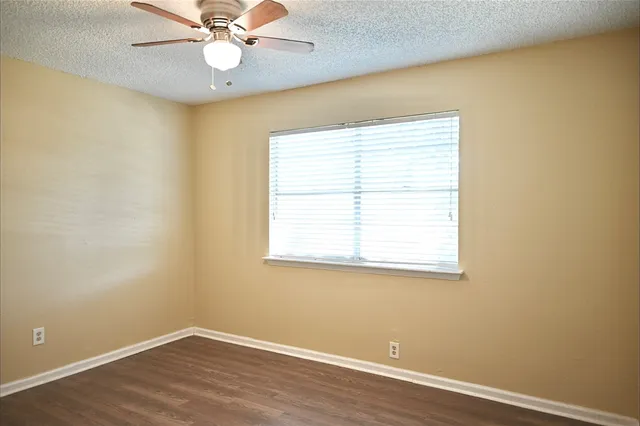 an empty room with wooden floor fan and windows
