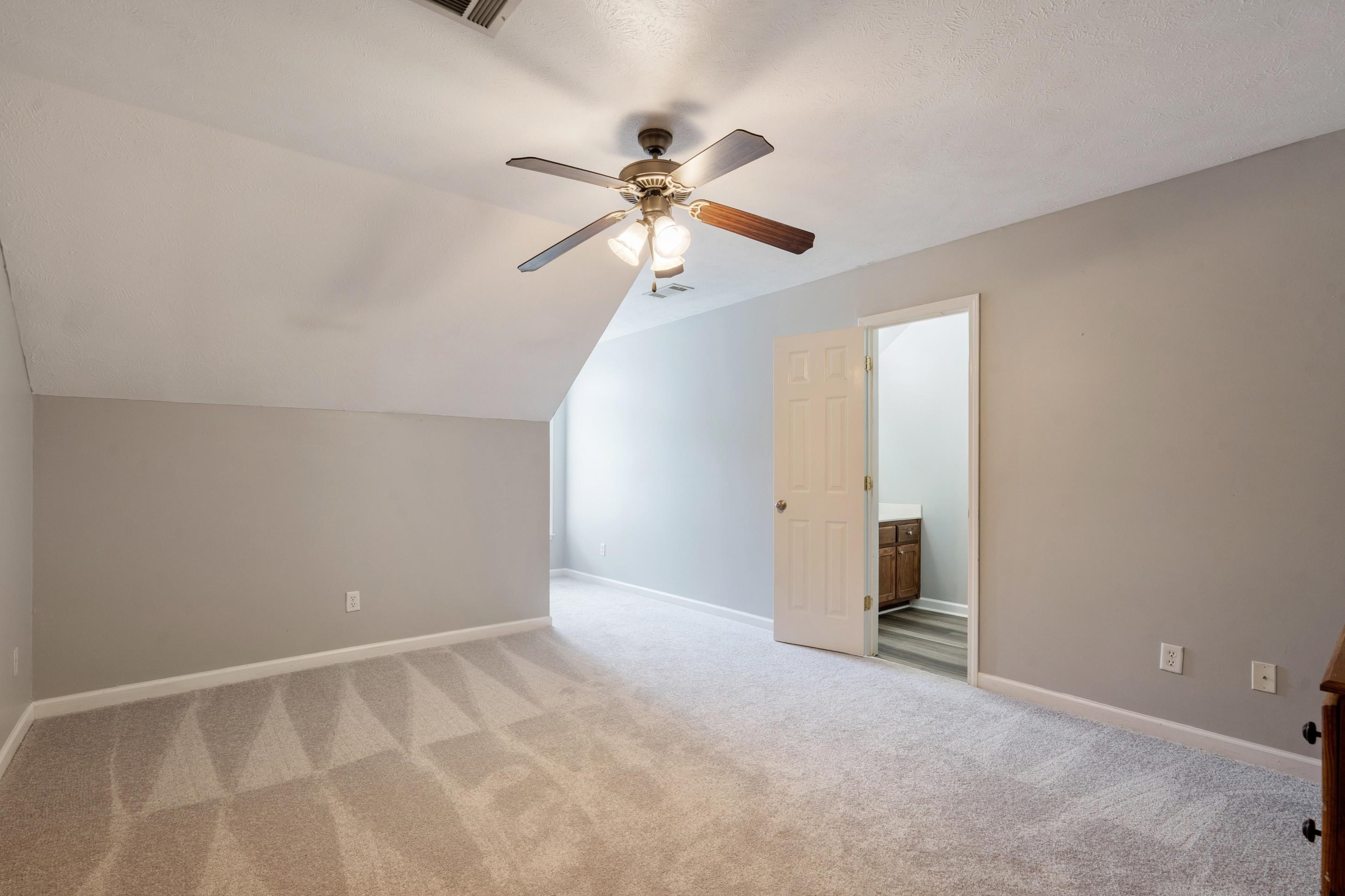 7757 Brunswick Road Millington, TN 38053 - Photo 19 of 40 Carpeted room with a ceiling fan, sloped ceiling detail, and a doorway revealing a vanity with wood-finish cabinetry
