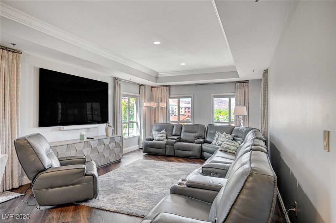 Living room with wood finished floors, a raised ceiling, ornamental molding, and recessed lighting