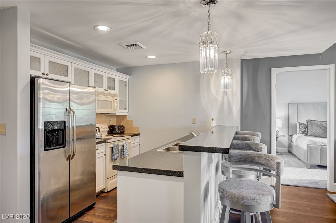 30 Strada Di Villaggio, Unit 250 Henderson, NV 89011 - Photo 11 of 52 Kitchen featuring a kitchen bar, glass insert cabinets, white appliances, recessed lighting, and dark wood finished floors