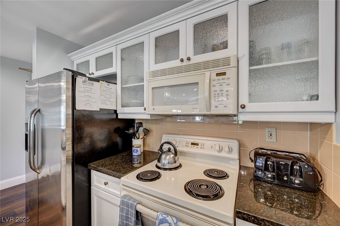 30 Strada Di Villaggio, Unit 250 Henderson, NV 89011 - Photo 14 of 52 Kitchen featuring white appliances, backsplash, dark stone countertops, white cabinetry, and glass insert cabinets