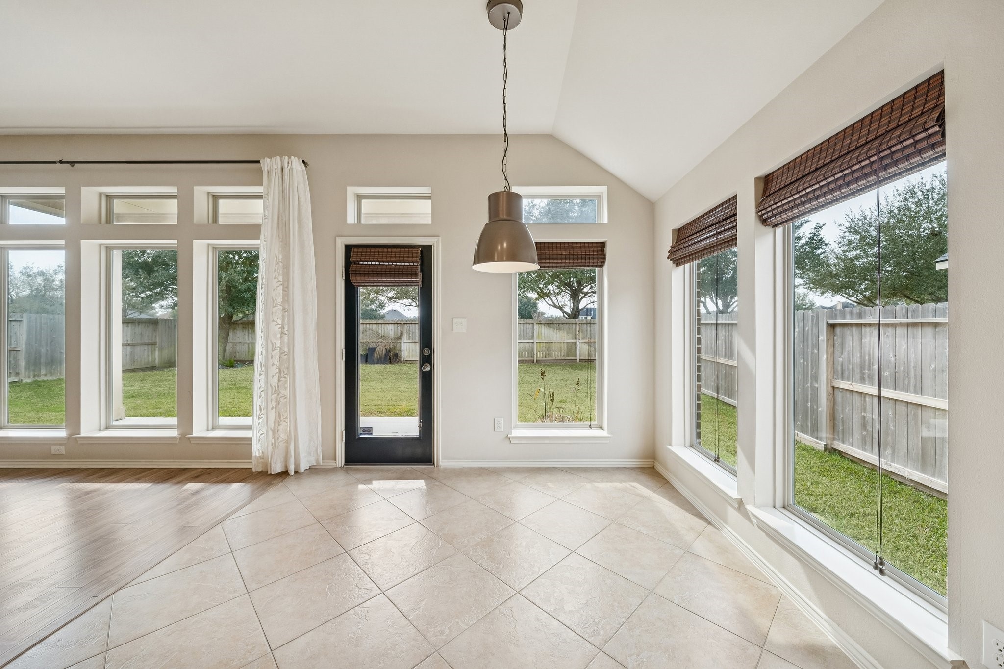 13014 Barkley Bend Lane Houston, TX 77044 - Photo 20 of 42 Sunlit breakfast nook features a vaulted ceiling and neutral tile flooring laid on a diagonal for a spacious feel. Large windows and a glass-paneled door frame views of the grassy backyard, while a contemporary pendant light anchors the space. Direct access to the covered patio makes transitioning to outdoor relaxation effortless in this open-concept layout.