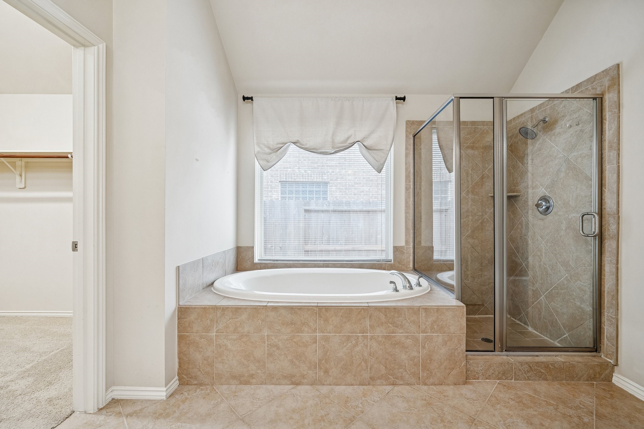 13014 Barkley Bend Lane Houston, TX 77044 - Photo 27 of 42 Retreat to this spa-inspired primary ensuite featuring a deep soaking tub positioned beneath a large window for a serene atmosphere. A glass-enclosed walk-in shower with floor-to-ceiling tile sits adjacent, while diagonal tile flooring extends into the expansive walk-in closet for seamless movement. Neutral tones and high ceilings enhance the sense of openness in this private sanctuary.