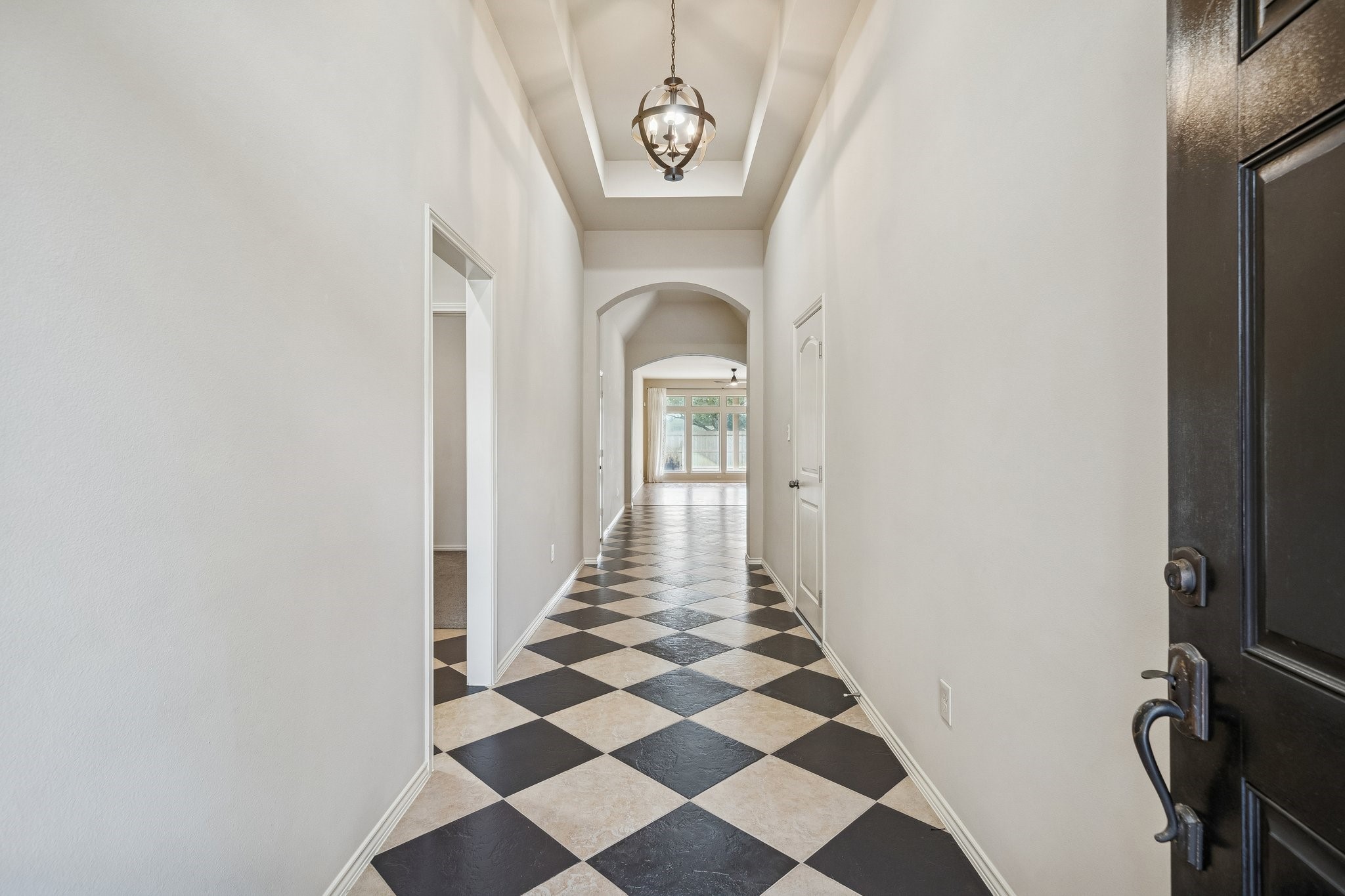 13014 Barkley Bend Lane Houston, TX 77044 - Photo 9 of 42 Checkered tile flooring in a bold diamond pattern creates a striking visual through the foyer, leading toward the arched transitions of the main living areas. A recessed tray ceiling features a contemporary globe chandelier, while neutral walls and arched doorways enhance the sense of architectural depth throughout this one-story layout.
