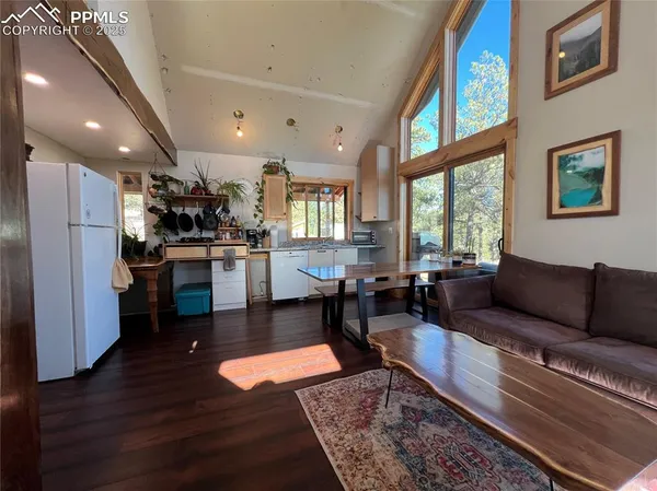 a living room with stainless steel appliances furniture wooden floor and a kitchen view