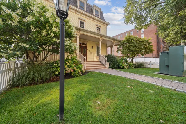 a view of a white house next to a yard with big trees