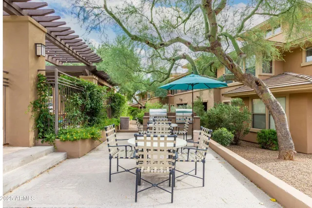 a view of a patio with table and chairs under an umbrella with large trees