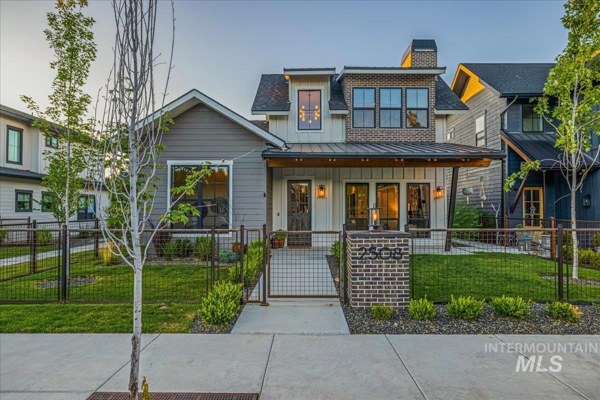 View of front of property featuring board and batten siding, covered porch, a fenced front yard, a standing seam roof, and a gate