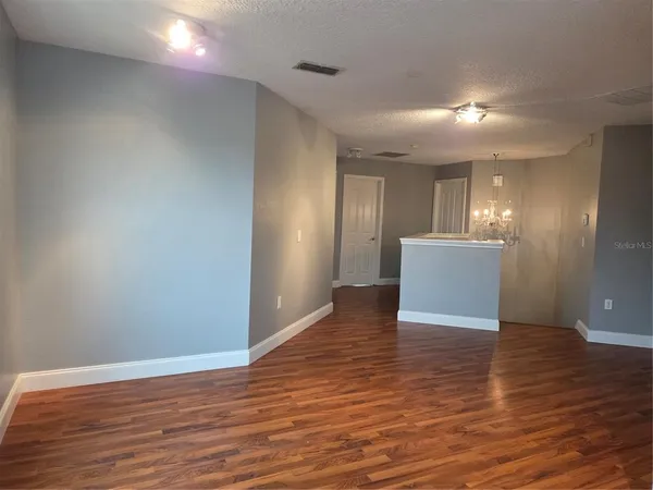 a view of an empty room with wooden floor and a kitchen