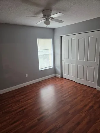 an empty room with wooden floor chandelier fan and windows