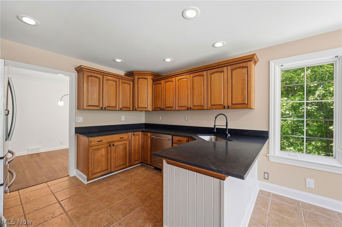 7750 Lewis Road Olmsted Falls, OH 44138 - Photo 18 of 50 Kitchen featuring wood cabinetry, dark countertops, a stainless steel dishwasher, and a window with exterior greenery