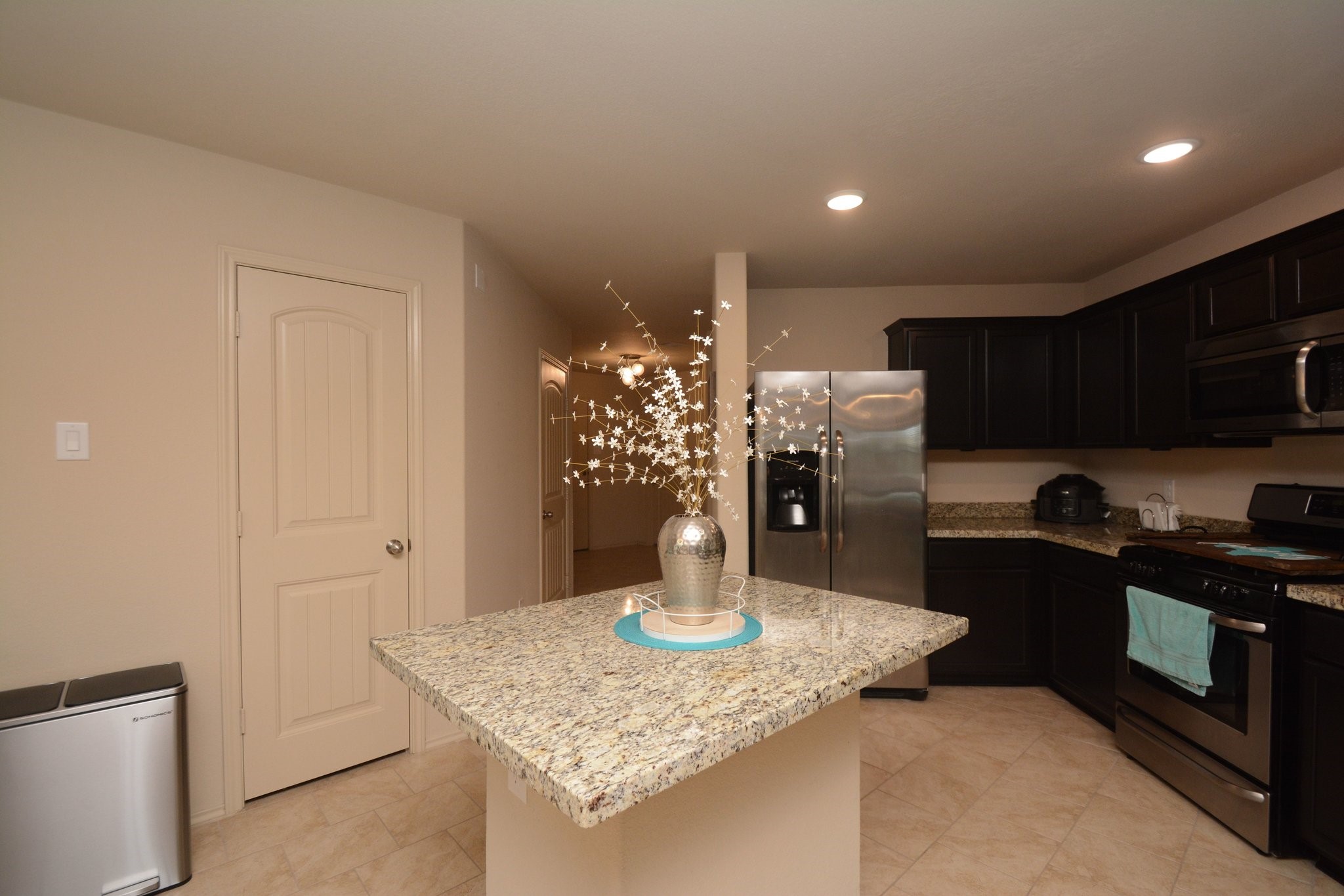 23318 Dukes Run Drive Spring, TX 77373 - Photo 8 of 41 This kitchen features modern stainless steel appliances, dark cabinetry, and a central island with granite countertops. The space is well-lit with recessed lighting and has a neutral tile floor, creating a warm and inviting atmosphere.