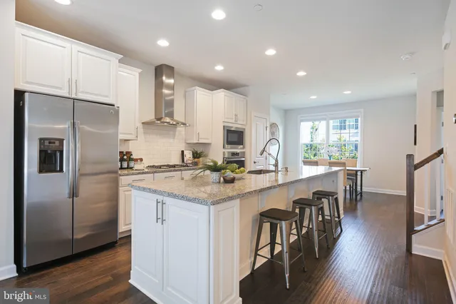 a kitchen with stainless steel appliances granite countertop a refrigerator a stove a sink a dining table and chairs