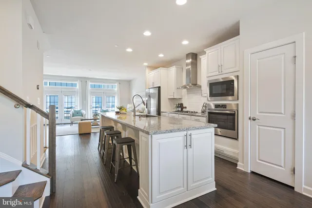 a kitchen with kitchen island granite countertop a stove a sink a refrigerator and white cabinets with wooden floor